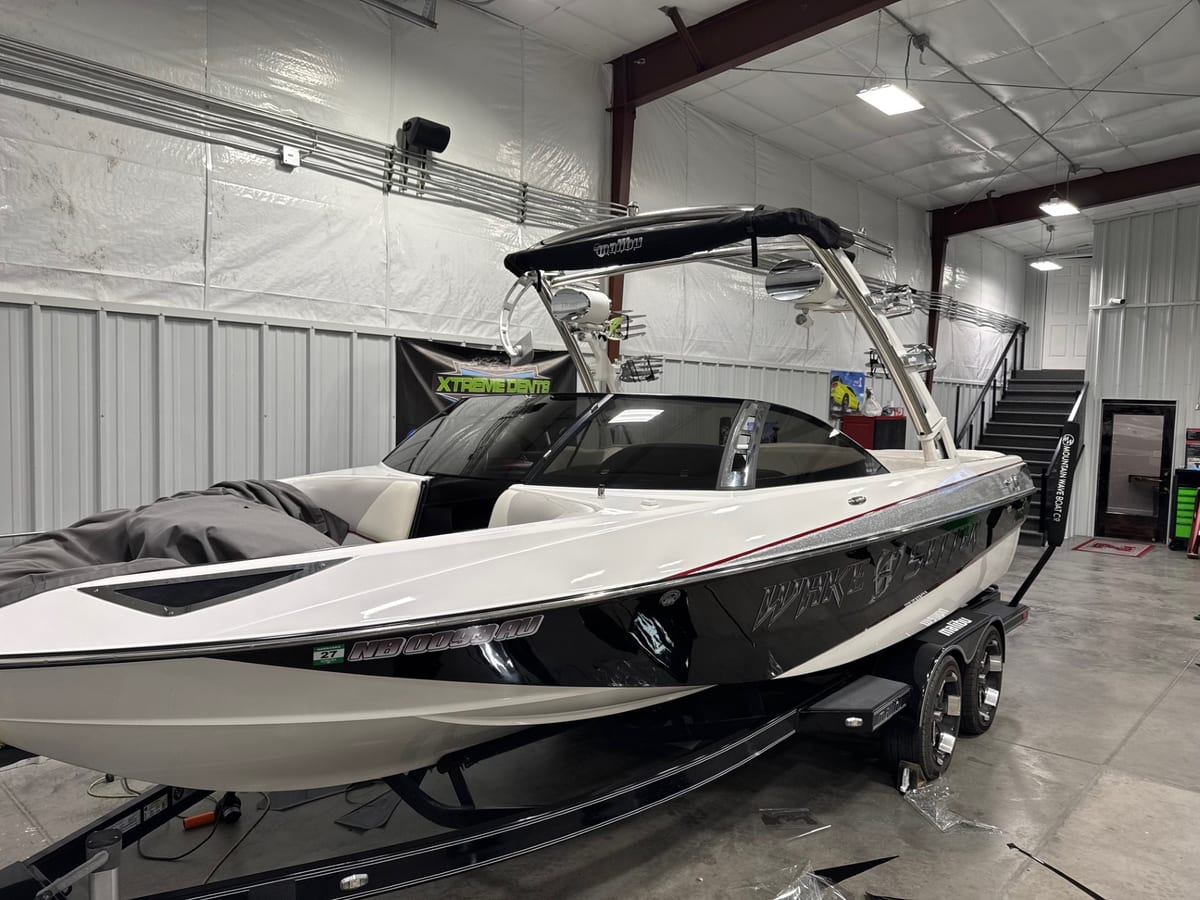White and black boat on a trailer with dark windshield glass inside a workshop.